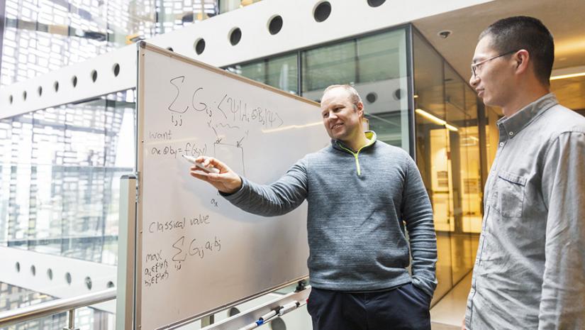 A/Prof Troy Lee (left) discusses quantum information theory with Prof Zhengfeng Ji (right) while writing on a whiteboard