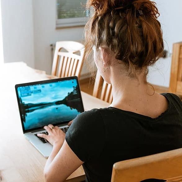 Woman sitting at a dining room table with her laptop in front of her.