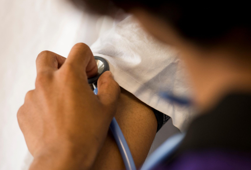 Health professional checks patient's pulse with stethoscope on arm