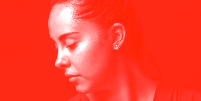 Image of a woman looking down and away from the camera against a red background