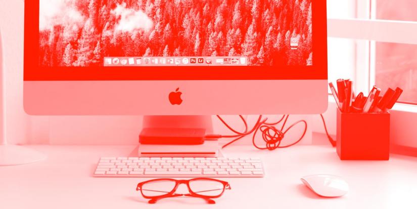 Red image of desktop computer with pens and glasses.
