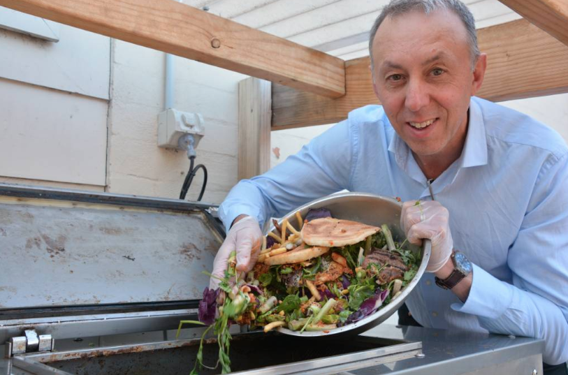 A man tips a bowl of food rubbish into an air drying machine