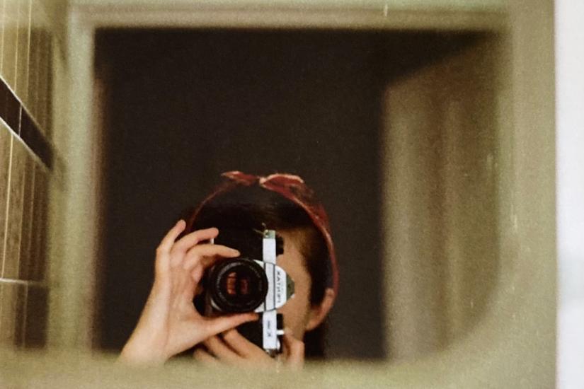 Anwen Crawford self portrait holding camera reflected in a mirror