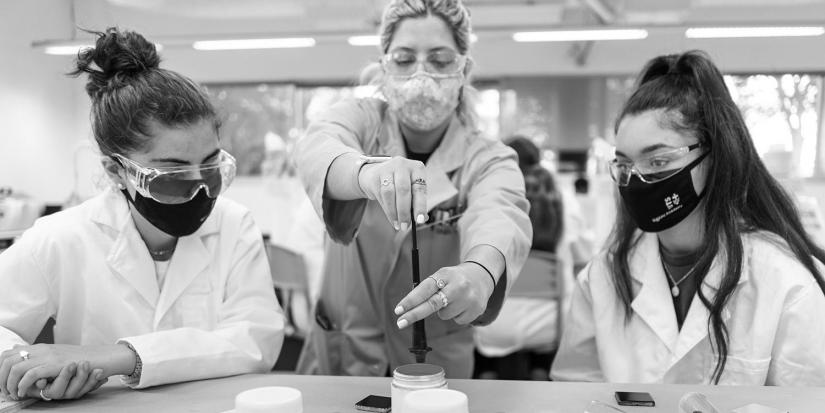 High school students wearing masks and safety goggles while doing an experiment in a lab.