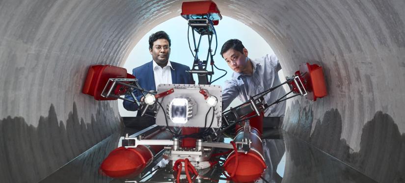 A robot with five arms in a tunnel and two researchers looking on