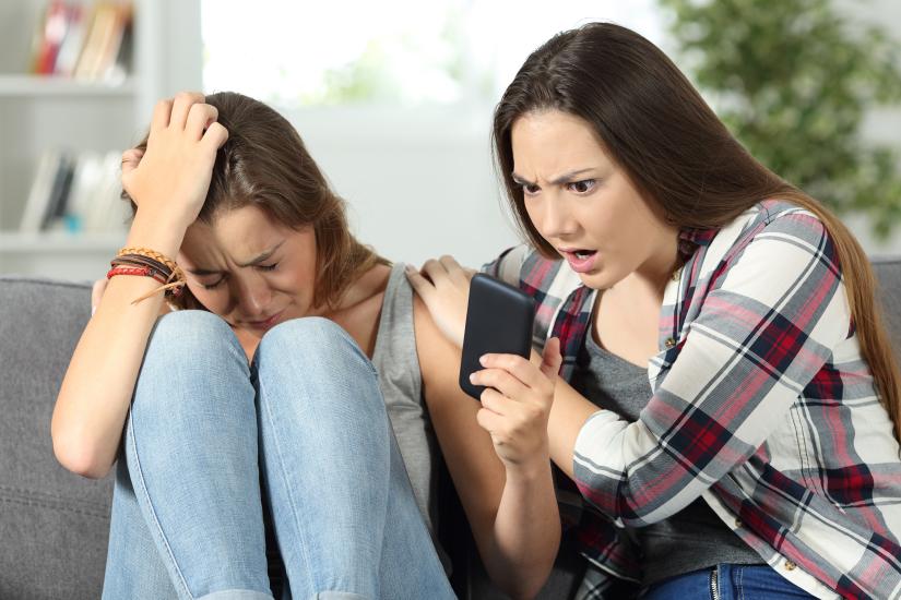 One girl in tears shows her phone to a friend who looks shocked