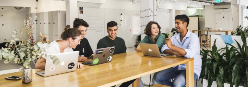 Five young people smiling as they sit around a table in front of their laptops