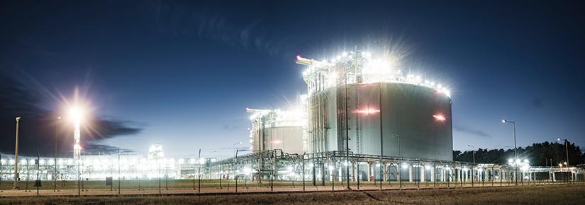 A liquefied natural gas storage facility at night with two storage tanks prominent in the foreground