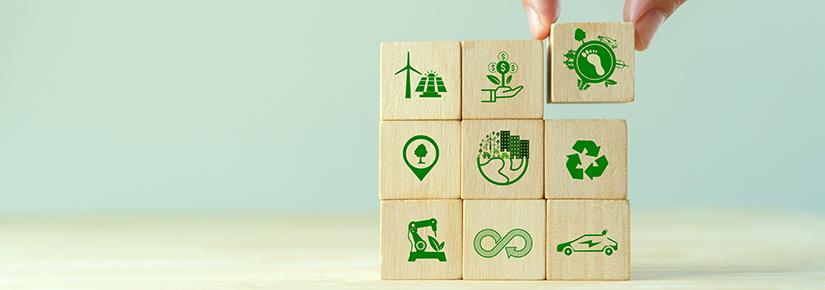 Stock picture of a hand placing wooden blocks in a square formation, each depicting a symbol of sustainable industry. 