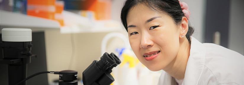 Dr Jiao Jiao Li stands at her microscope in her lab at UTS