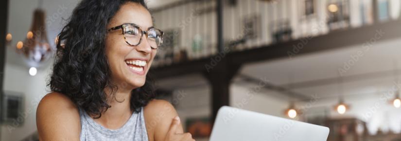 A woman smiles widely as she looks as a computer screen.