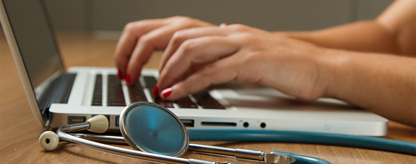 Woman's hands on laptop keyboard with stethoscope to the side in foreground