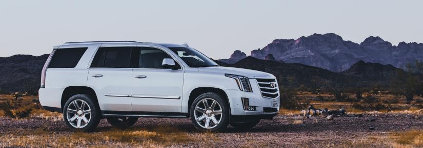 a white SUV sits on a dirt path with mountains in the background.