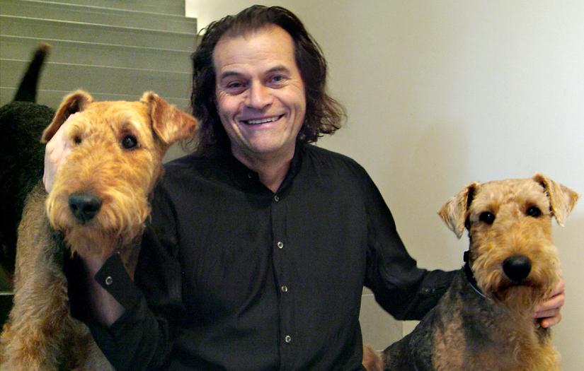 Brian Sherman in a black shirt sitting on stairs smiling and looking at the camera with his two dogs