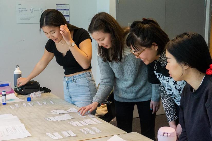 Four women of Asian appearance collaborate around a table looking at paper cut-out tags