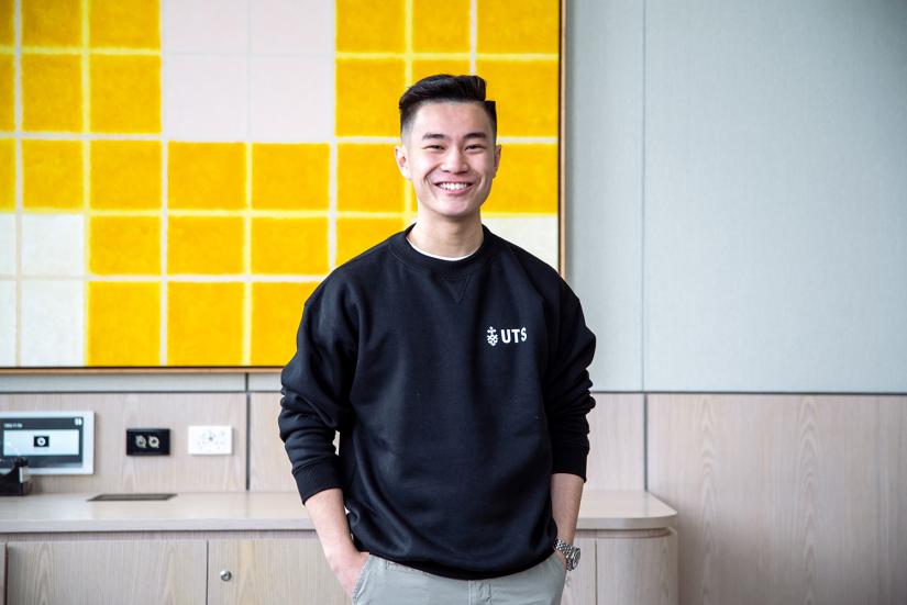 UTS student Kurt Cheng smiling while wearing a UTS branded black crew neck jumper.