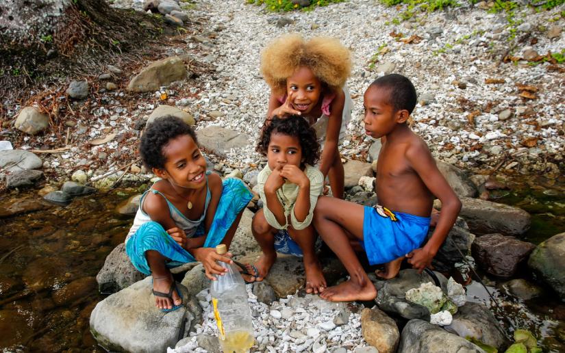 A group of children sit on rocks by a river in Fiji.