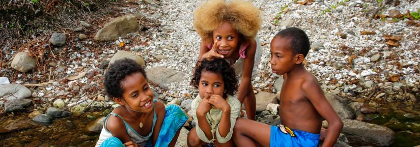 A group of children sit on rocks by a river in Fiji.