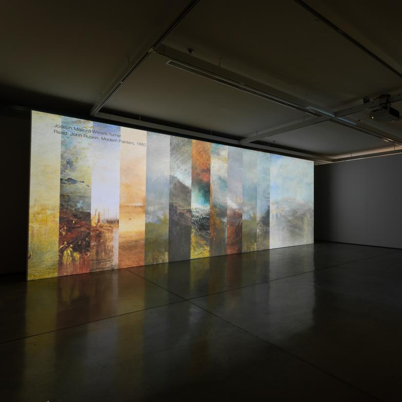 A large projector screen in a darkened room shows a composite image of cloud from Turner paintings