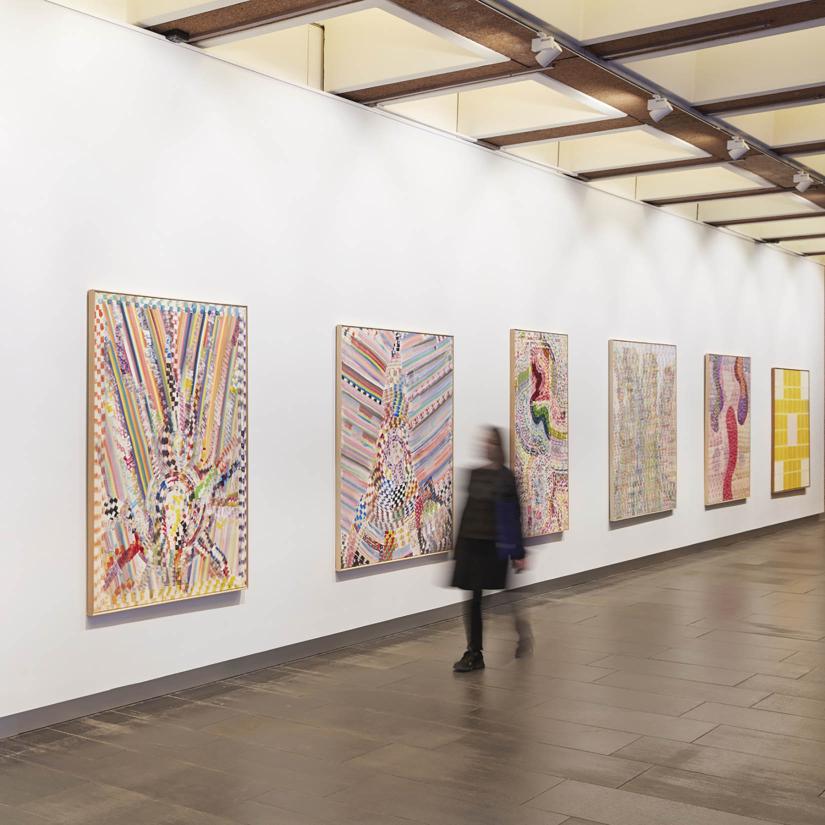 A person walks past a wall of colourful paintings, they are blurred as they walk.