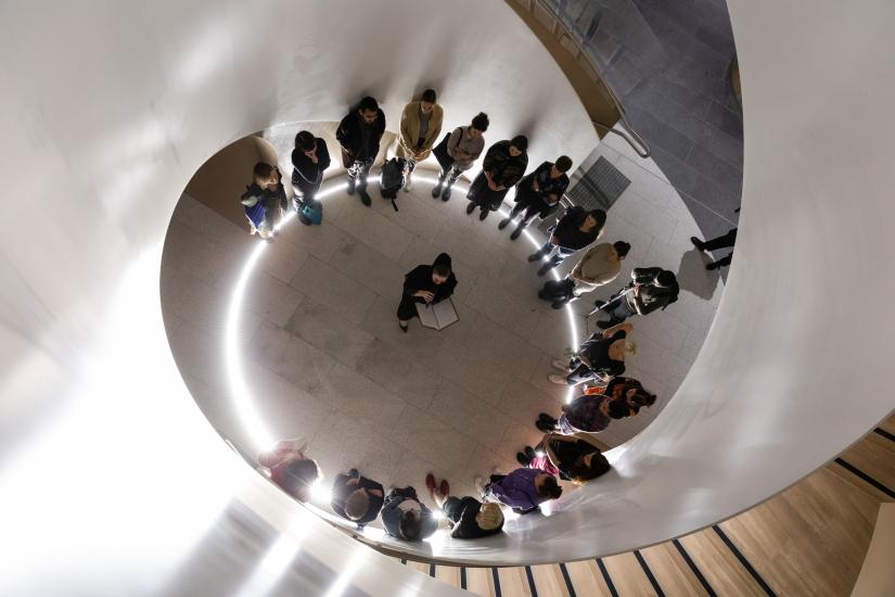 An aerial view of people standing in a circle. They stand in the atrium of a spiral staircase. 
