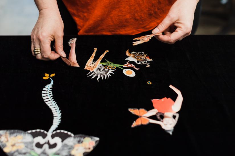 A person's hands place paper cutouts on a piece of black fabric. 
