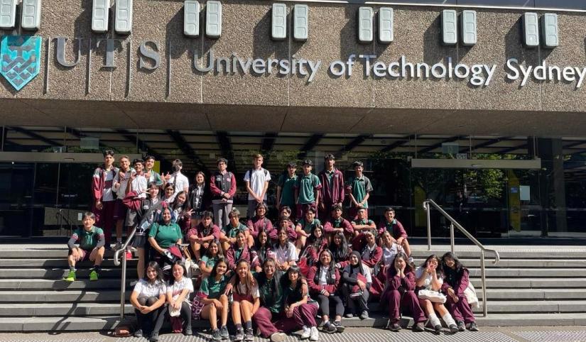Outdoor daytime group photo of high school students in uniform and teachers, on the steps of UTS Tower building.