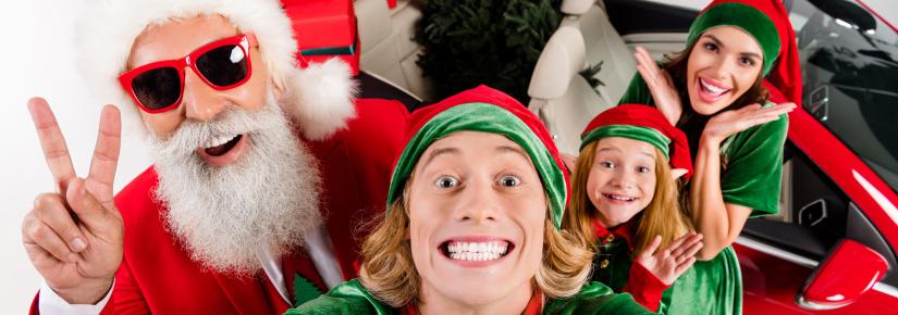 A man takes a selfie with Santa with a woman and young girl in the background.
