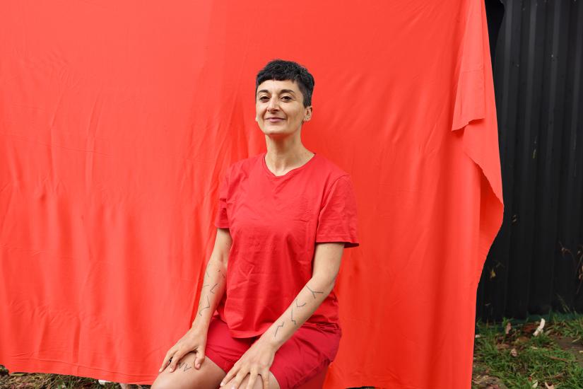 A woman dressed in red sits upright in front of a red backdrop