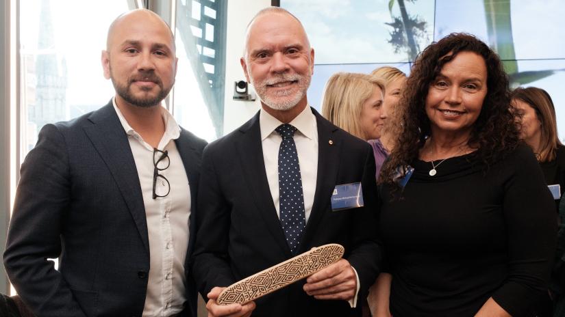 Adam Bray, Professor Michael McDaniel AO, and Professor Robynne Quiggin smile as they pass the College message stick.