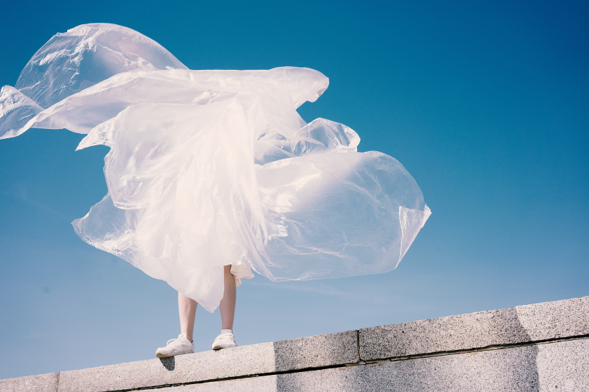 Person standing on wall obscured by white material in shape of a cloud, seen against a blue sky