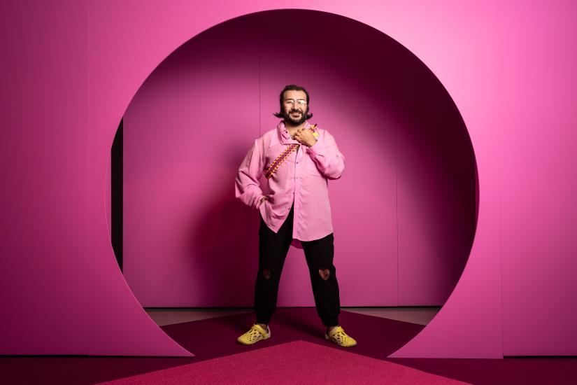 A person in a pink shirt stands in round doorway painted pink