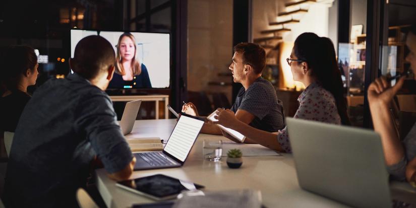 a group of colleagues sitting around a conference table and video conferencing with a person on a screen