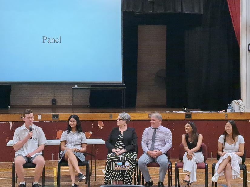 Panel of students and teachers inside a high-school gym.