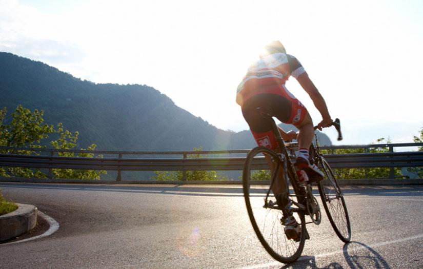Cyclist approaching a bend on a mountain with the sun reflecting off his helmet