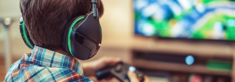 A child wears headphones and holds a remote controller to play video games.