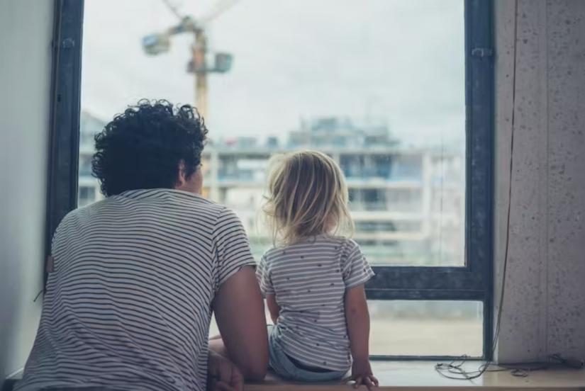 An adult and child look out of a window in an apartment