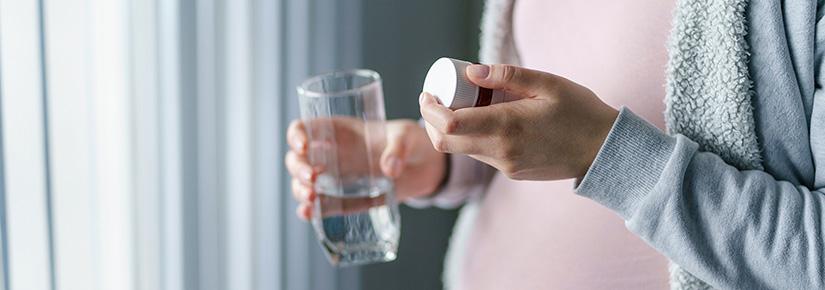 Pregnant woman holding pill bottle and glass of water