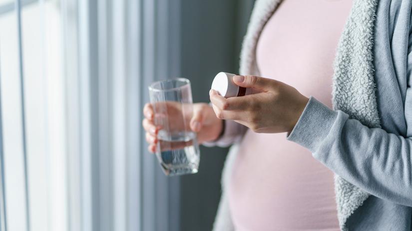Pregnant woman holding a pill bottle and glass of water