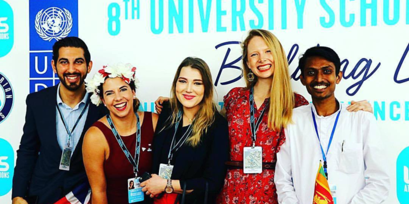 Alli Devlin poses with four other students, second from right. They stand against a blue and white backdrop.