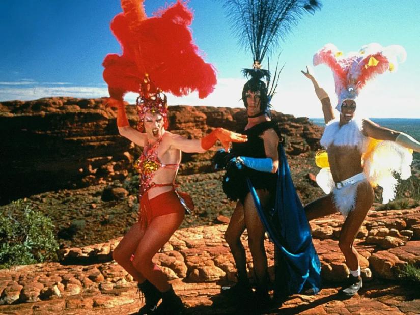 A still from 'Priscilla, Queen of the Desert', where three drag queens stand a top a rocky mountain in the Australian outback.