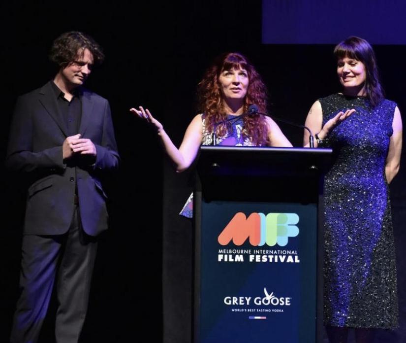 Melanie (centre) stands on stage speaking at a lecturn