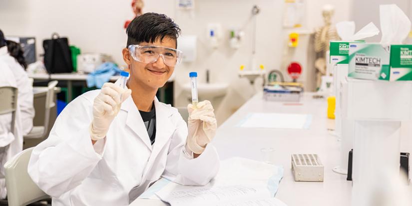 Male high school students in UTS science lab wearing a lab coat and glasses.