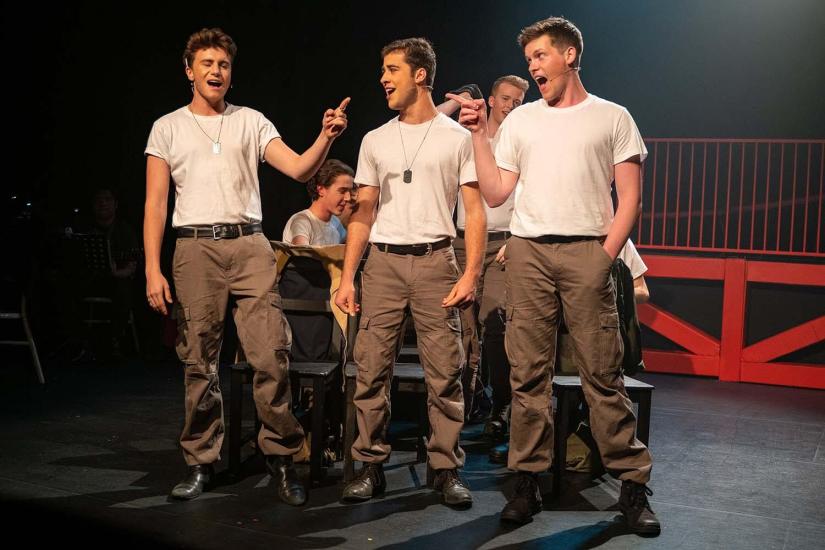 Three students in army uniforms perform on stage