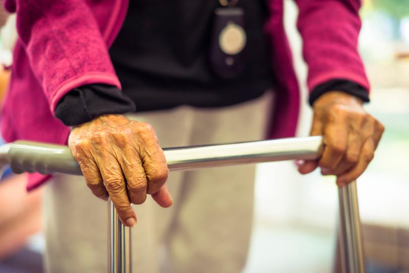 An older person stands with the assistance of a walking frame.