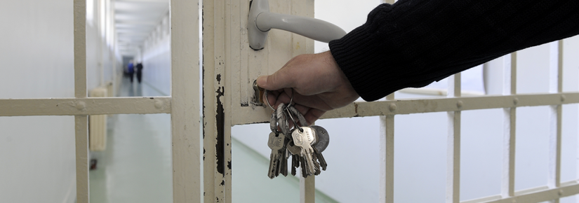 A hand locks a prison gate