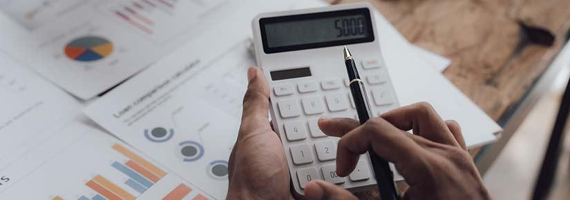 an individual uses a calculator, finance documents and graphs in the background