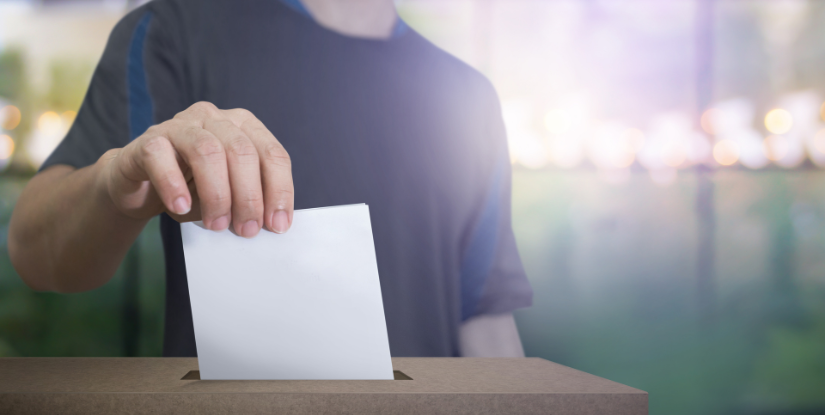 A man's hand placing a vote into a ballot box
