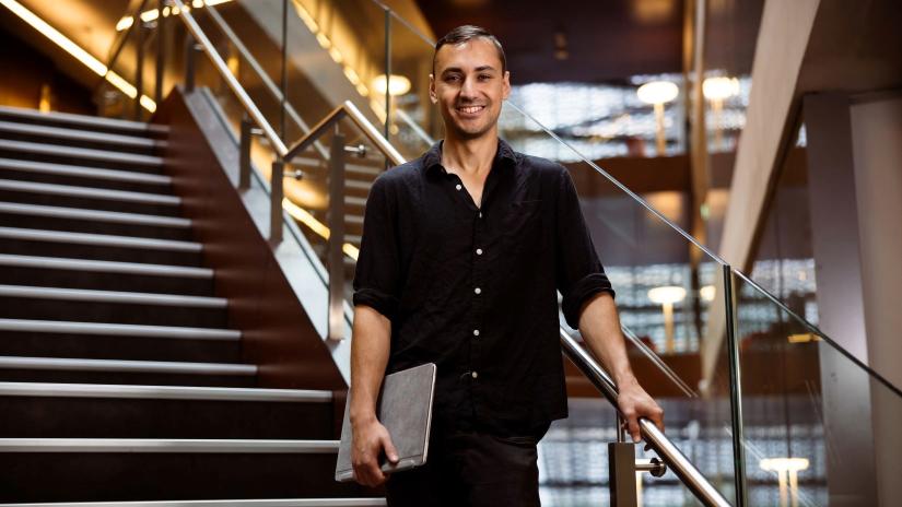 QSI SQA PhD Student Mauro Morales standing on a staircase in UTS Building 11, smiling and holding his laptop. 