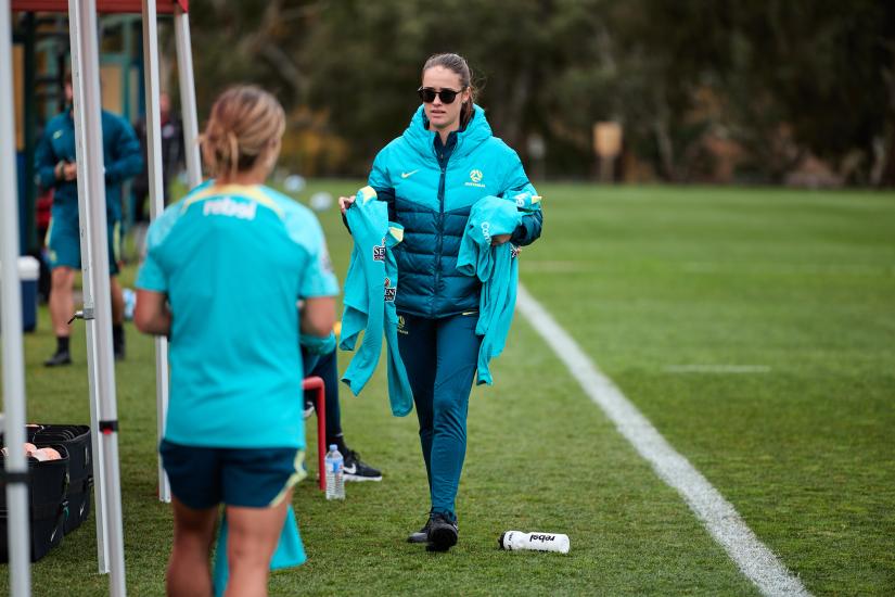 A woman dressed in a teal uniform on the sidelines of a football pitch.